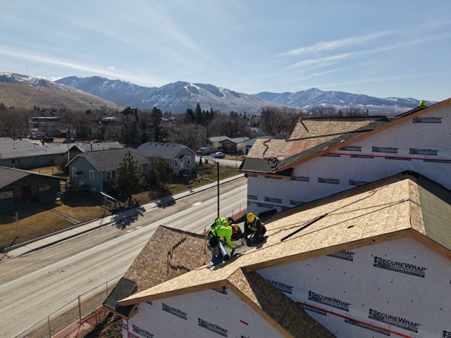 Western Montana Roofing crew installing a roof with snow-capped mountains behind