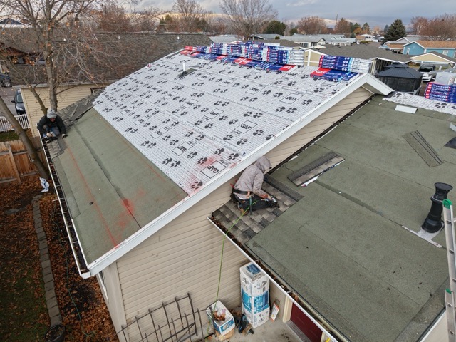 Aerial view of two workers installing synthetic underlayment and shingles with bundles staged for installation