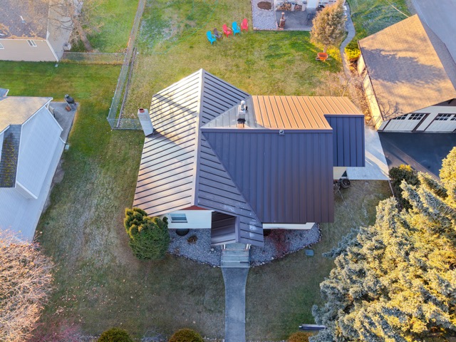 Modern home with a standing seam metal roof surrounded by green lawn and trees
