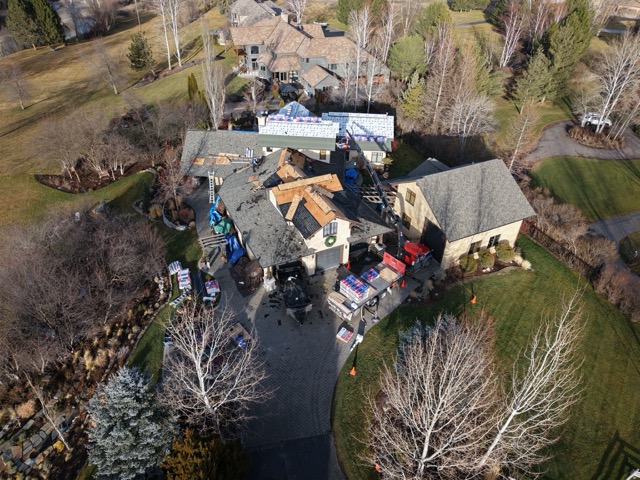 Aerial view of a large western Montana home undergoing roof replacement, with exposed decking and stacked shingle bundles