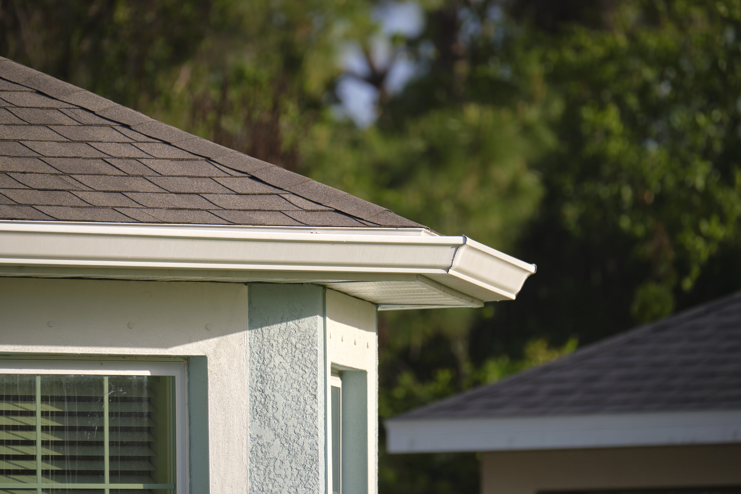 Close-up of a house corner with brown asphalt shingles and a white rain gutter