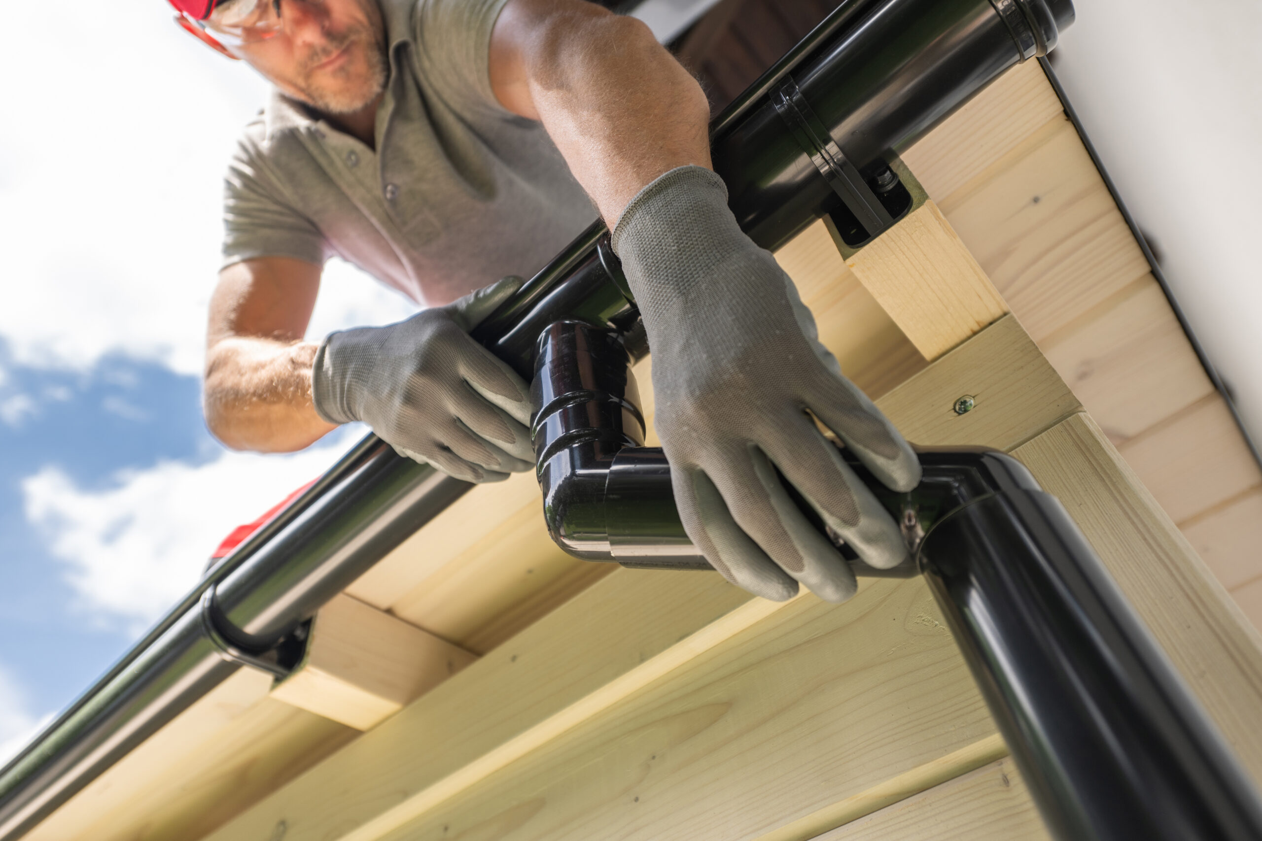 A man wearing gloves installing a black gutter system on a wooden roof