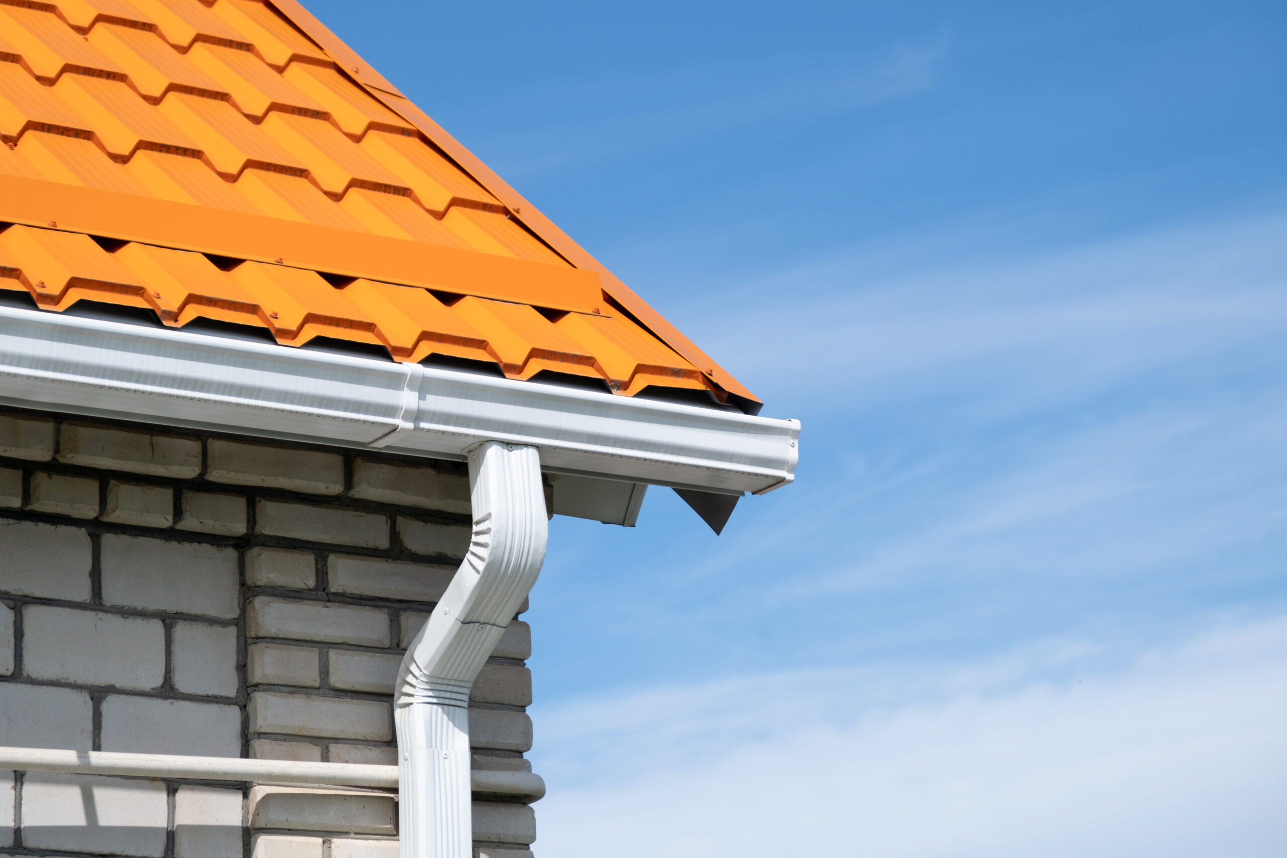 Close-up of a new white gutter on an orange metal roof against a blue sky
