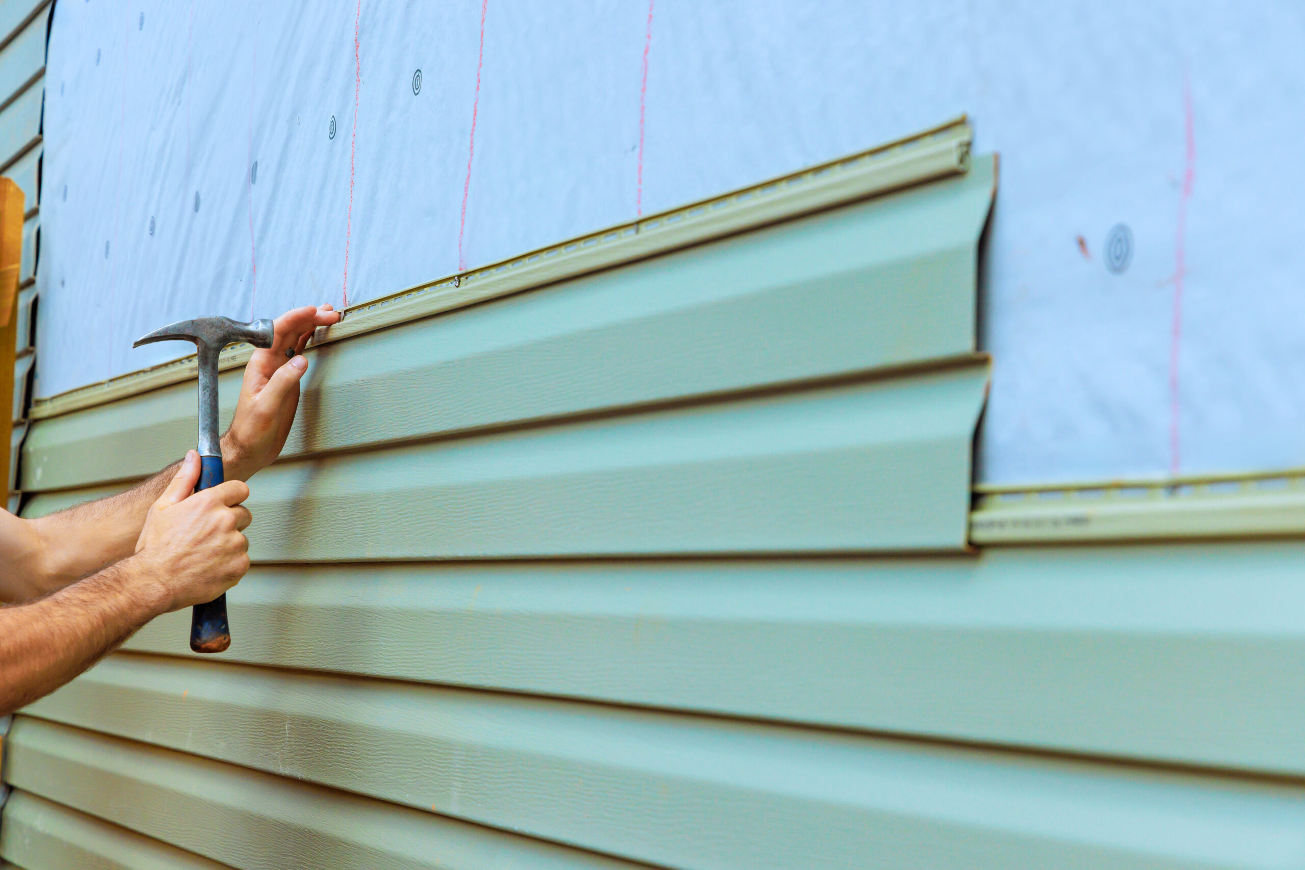 A construction worker installing new vinyl siding on a house