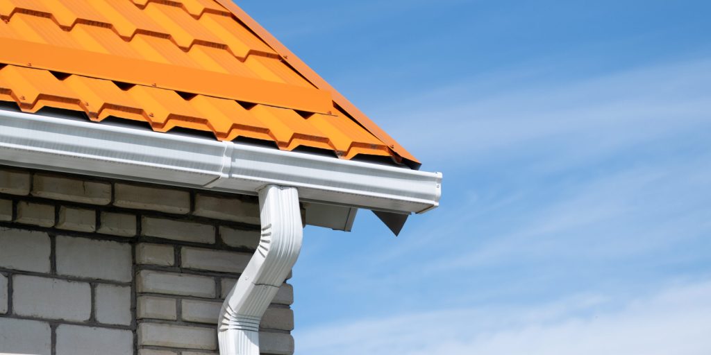 Close-up of a new white gutter on an orange metal roof against a blue sky.
