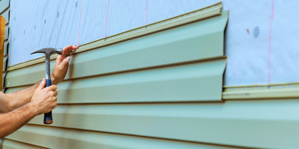A construction worker installing new vinyl siding on a house.